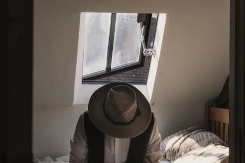 A man looking down wearing a fedora hat and waistcoat sitting on a bed Stock Photos