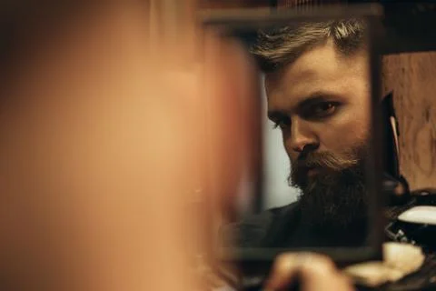 Man looking herself in the mirror while sitting in chair at a barbershop Stock Photos