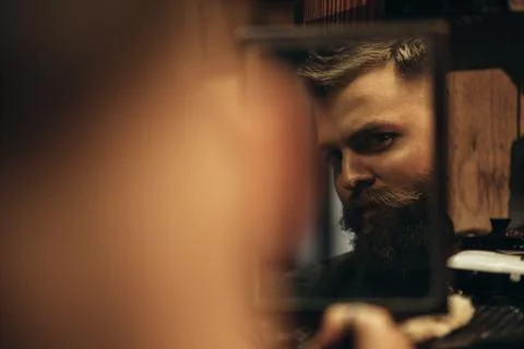 Man looking herself in the mirror while sitting in chair at a barbershop Stock Photos