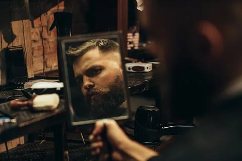 Man looking herself in the mirror while sitting in chair at a barbershop Stock Photos