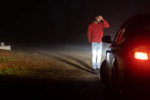 Man looking at his broken down car on a road one foggy night Stock Photos