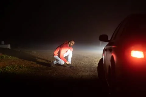 Man looking at his broken down car on a road one foggy night Stock Photos