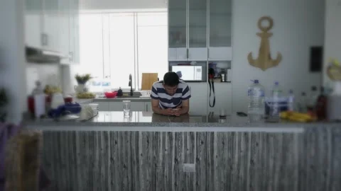 A man looking at his cell phone in the kitchen while waiting for food to boil in 库存影片 185331014