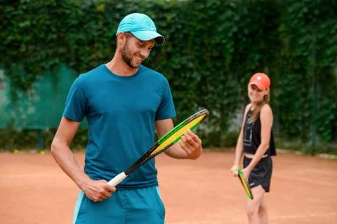 Man looking at his racket, while woman smiling in the background. Stock Photos