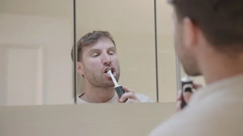 Man looking at his reflection in the mirror while brushing his teeth in the Stock-Footage 335201161