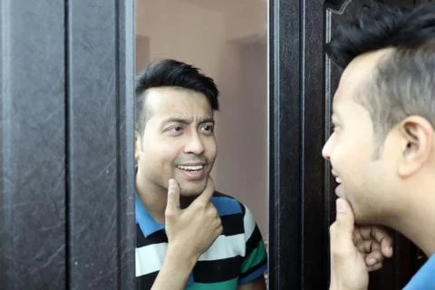 A man looking at his reflection in mirror and making smile gesture Stock Photos