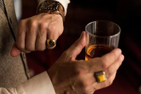 Man looking at his watch. Ring on the little finger. Holding a glass of whiskey. 库存照片