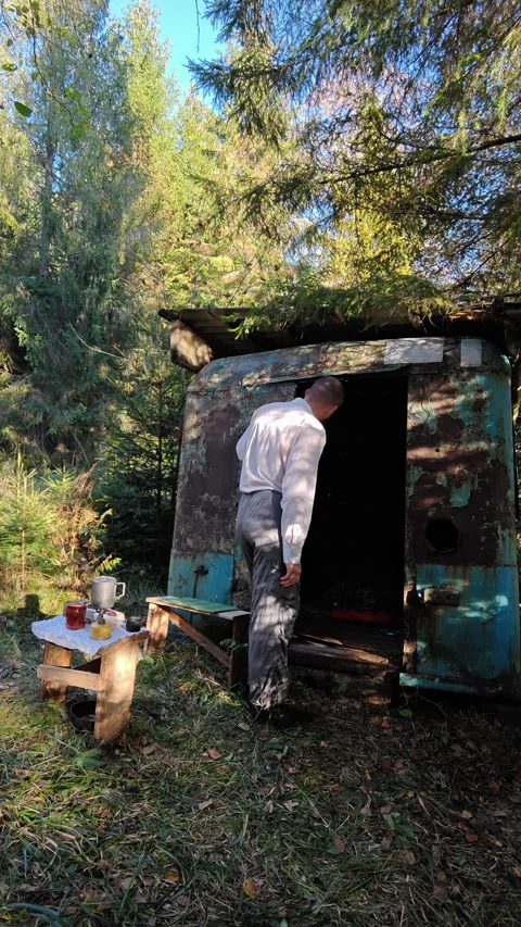 Man looking inside old abandoned metal trailer house in forest Stock Footage 348160213