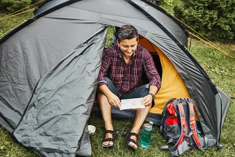 Man looking at map while planning next trip. Man relaxing in tent at campin.. Stock Photos