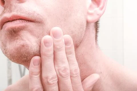 Man looking in mirror and applying product to skin on face in the bathroom Stock Photos