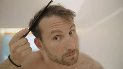 Man looking in the mirror, combing his hair, and then making a funny, happy face Stock Footage 335201108