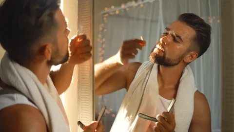 Man  looking in the mirror, smoking a cigarette and shaving his beard 動画素材 116334744