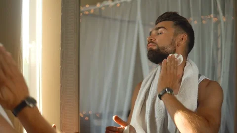 Man  looking in the mirror, smoking a cigarette and shaving his beard 動画素材 116334760