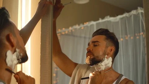 Man  looking in the mirror, smoking a cigarette and shaving his beard 動画素材 116334969