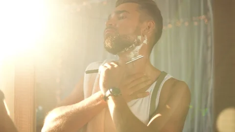 Man  looking in the mirror, smoking a cigarette and shaving his beard 動画素材 116334973