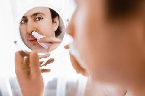 Man looking in a mirror using an electric trimmer for nose hair removal. A .. Stock Photos
