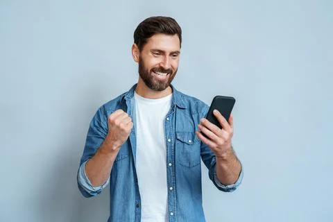 Man looking at mobile phone screen gesturing yes with clenched fist over blue Stock Photos