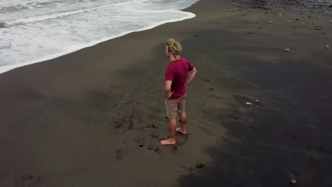 Man looking in ocean on black sand beach Stock Footage 157908198