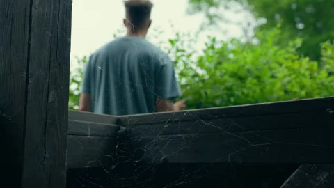 Man Looking Out Through Wooden Structure with Cobwebs and Green Foliage Stock Footage 339034032