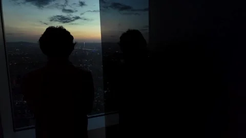 Man Looking Out Window at City After Sunset – Cinematic Urban Night Scene Video stock 308013842