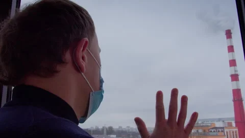 Man looking out of a window at poisonous smoke coming out of a factory chimney Stock Footage 307596424