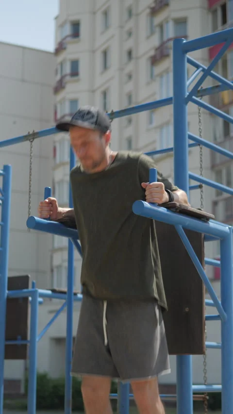 Man looking at phone while exercising on horizontal bars. vertical video Stock Footage 313359242
