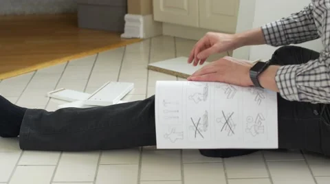 Man looking for pieces while reading instructions for flat pack furniture Stock Footage 56072431