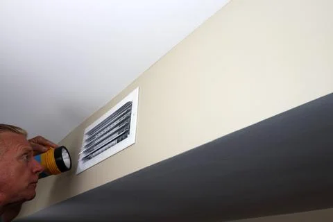 Man Looking into a Rectangle Home Wall Vent with a Flashlight Stock Photos