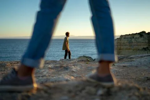 Man looking at seascape while standing on cliff seen through girlfriend legs Stock Photos