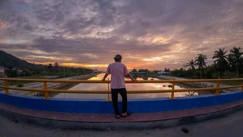 Man Looking at Sunset from Bridge Over River 스톡 사진