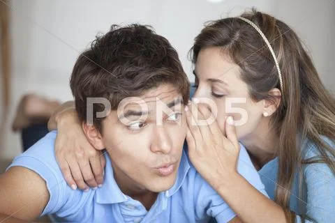 A man looking surprised at what his girlfriend is whispering in his ear Stock Photos