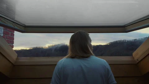 Man looking through attic window enjoying sunrise morning light at home Stock Footage 332557086