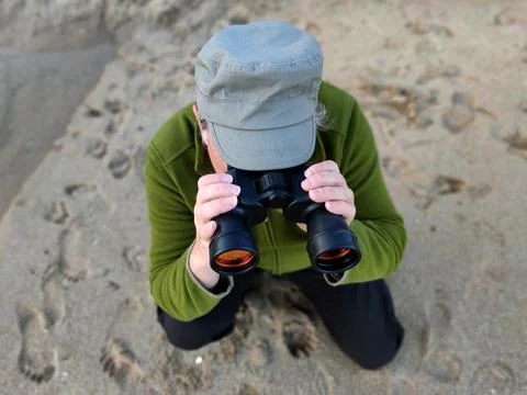 Man looking through binoculars sitting on the sand, top view Stock Photos