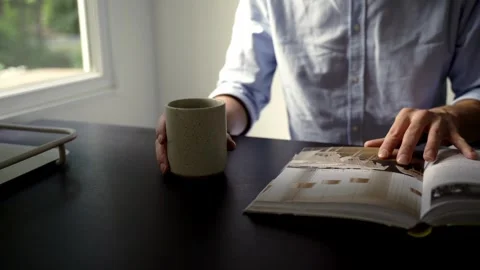 Man looking through cook book whilst holding coffee mug Видео 261079298