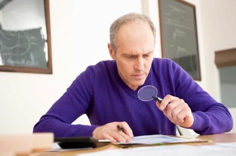Man looking through a magnifying glass while filling his tax form Stock Photos