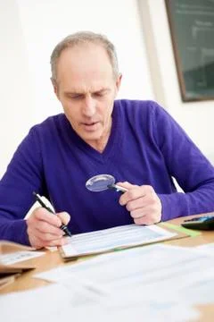 Man looking through a magnifying glass while filling his tax form Stock Photos