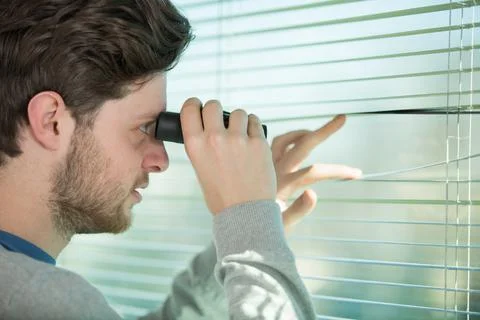 Man looking through window blind with binoculars Stock Photos