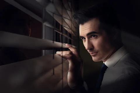 Man looking through window blinds at stranger in darkness. Paranoia concept Stock Photos