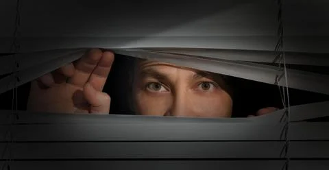 Man looking through window blinds into darkness. Paranoia concept Stock Photos