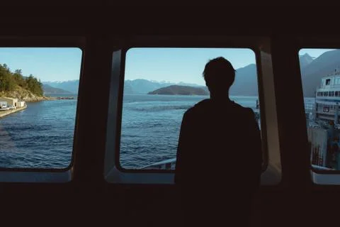 Man looking through window on ocean and mountains Stock Photos