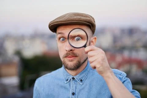 Man looking using magnifying glass outdoor with urban view 库存照片