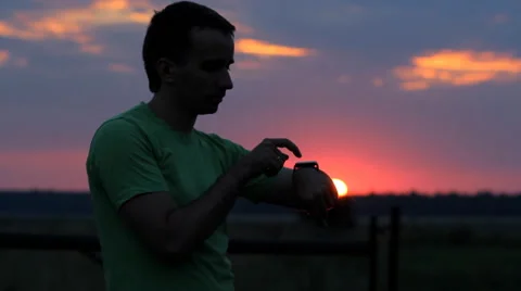 A man looks and touch smart watch at sunset. Beautiful red sky and the sun Stock Footage 65025418