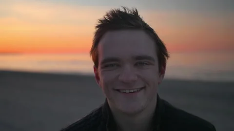 A man looks at the camera against the backdrop of a sunset and smiles Stock Footage 197884265