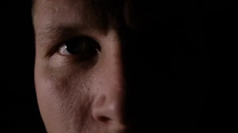 A man looks at the camera in the dark. Close-up eye. Only half of the face is Stock Photos