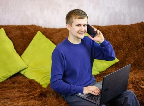 A man looks at the camera, talking on the phone and working at the computer. Stock Photos