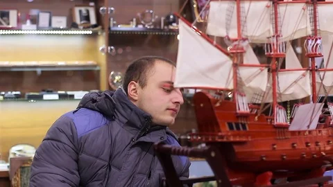 Man looks closely at Decorative ship in the shop Stock Footage 72076090