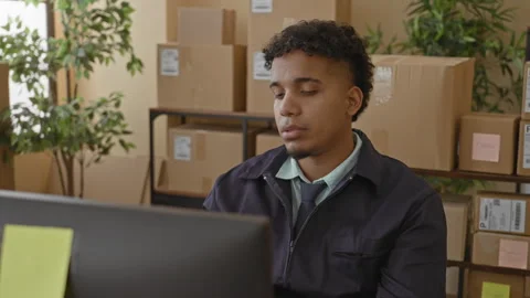 Man looks at computer screen with stacked packages and cardboard boxes in a.. Stock Footage 337418159