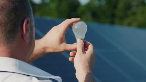 A man looks at an electric light bulb against the background of solar power Stock Footage 132272060