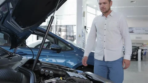 Man looks at the engine compartment of the car at the dealership Stock Footage 248914190