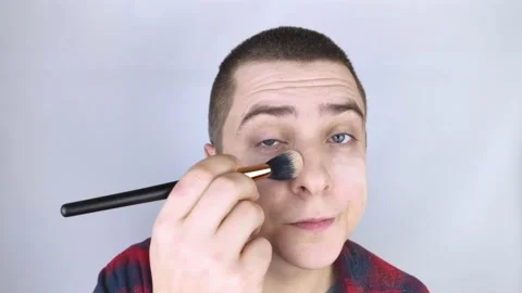 The man looks into the frame and uses powder. Close-up of a guy putting makeup o Stock-Footage 146360662